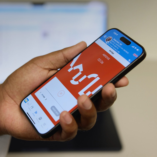 手に持ったiPhoneに、患者と医療従事者の会話をテキストにして診療記録を作成するAbridgeアプリが表示されている