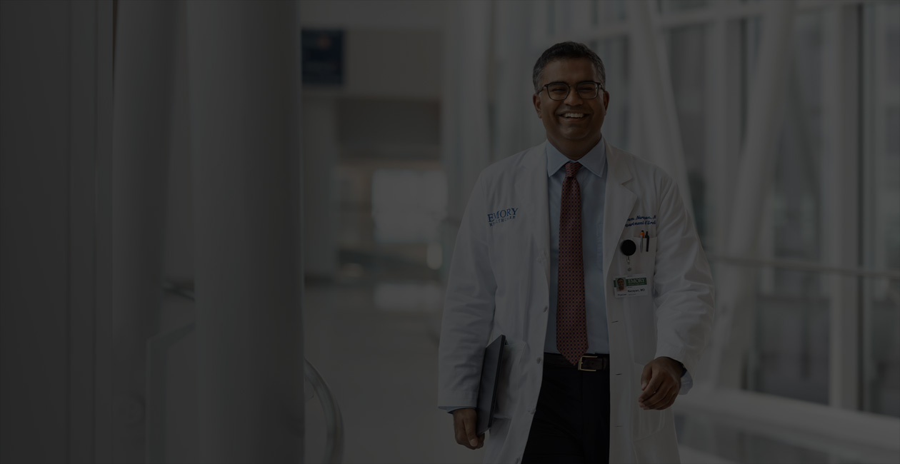 Médico segurando um MacBook embaixo do braço direito enquanto caminha.