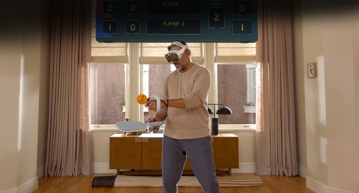 صورة لرجل يرتدي جهاز Apple Vision Pro ومعه وحدة تحكم Sony PlayStation VR2 Sense٫، وهو يلعب لعبة Pickle Pro، وتظهر لوحة النتائج المكانية فوق رأسه