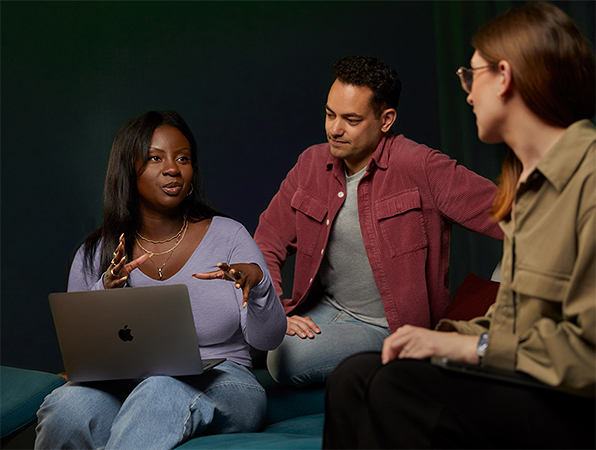 Installés dans un canapé, trois membres de l’équipe Logiciels et services d’Apple – l’un d’eux avec un MacBook – discutent.