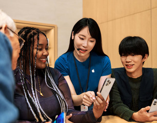 Apple StoreのスタッフがiPhoneを手に持った参加者と話し、ほかの2人の参加者もそのiPhoneをのぞき込んでいる
