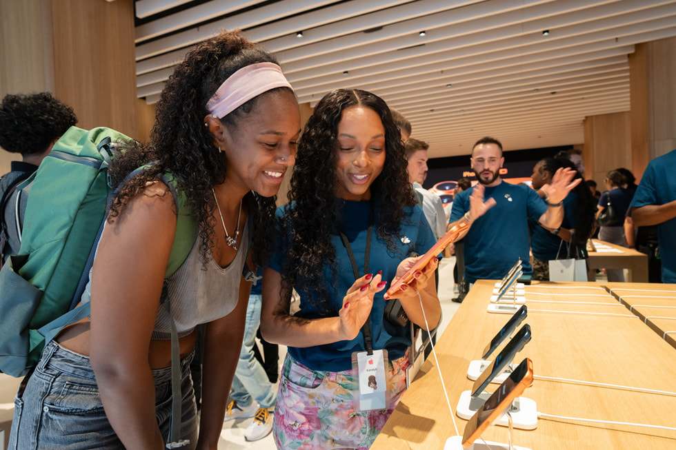 A team member shows a customer iPhone 17 Pro in cosmic orange at Apple Downtown Detroit.