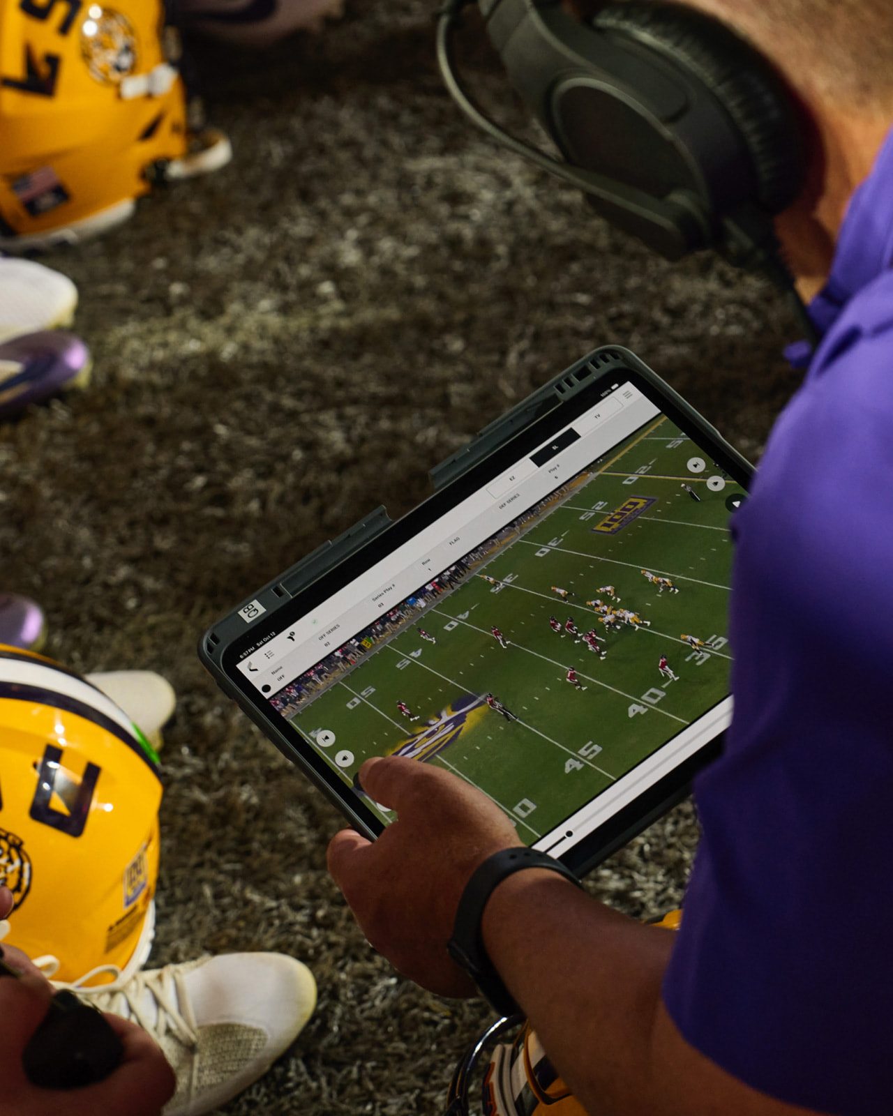 College football players and coaches look at iPad on the sideline during a game.