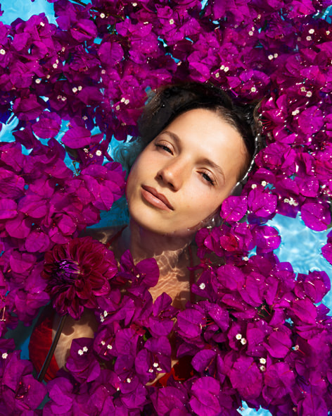 A woman in a swimming pool, surrounded by a blanket of bougainvillea flowers. Shot on iPhone 16 Pro Max by Clementine Bourke.