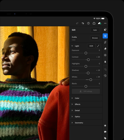 Vista frontal do iPad Pro, preto sideral, colocado na horizontal, o ecrã mostra a edição da fotografia de uma pessoa com uma camisola colorida, com o menu de ferramentas e efeitos aberto à direita