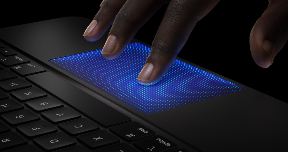 Animação de uma mão a passar os dedos sobre o trackpad do Magic Keyboard, o dedo indicador com uma sombra azul mostra a ação de toque, para exemplificar o feedback tátil
