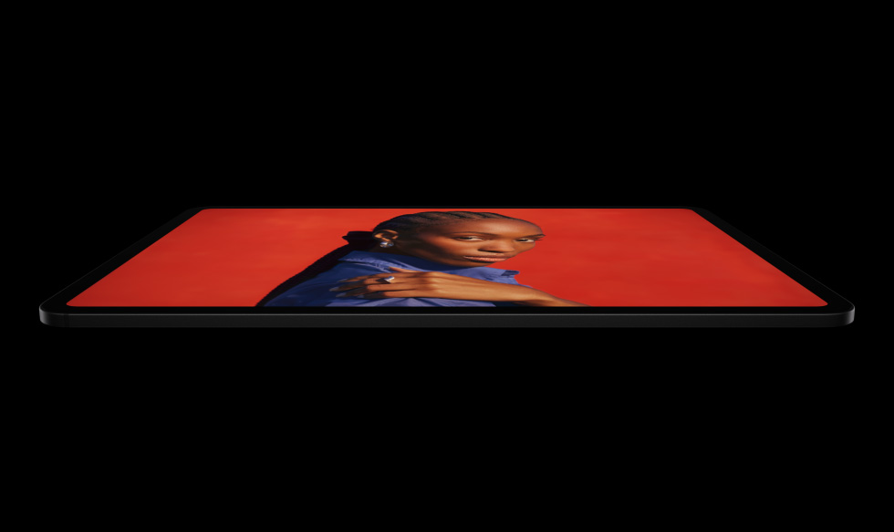 橫向放置的太空黑色 iPad Pro 機身側面,展示圓角設計與黑色顯示器邊框,顯示器展示在鮮豔的紅色畫面中,一個身穿藍色襯衫的人手搭在肩上擺出姿勢